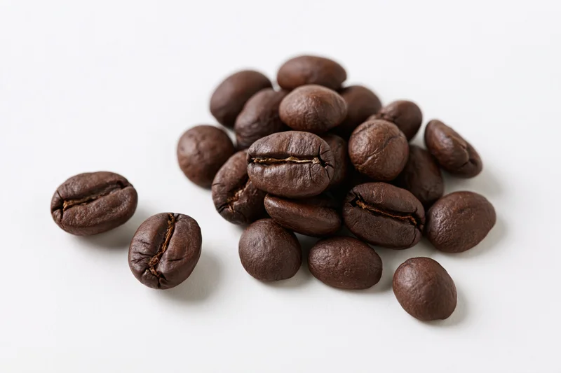 Roasted coffee beans scattered loosely on a white surface