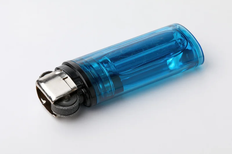Translucent blue plastic disposable lighter lying on white surface with metal ignition wheel and cap visible