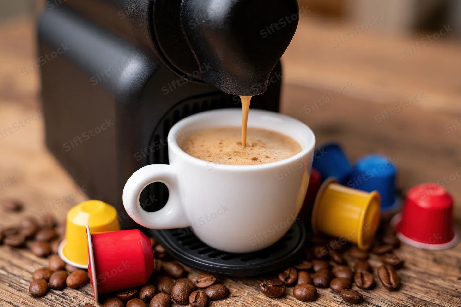 Coffee machine brewing espresso into a white ceramic cup on a wooden table surrounded by coffee capsules and beans