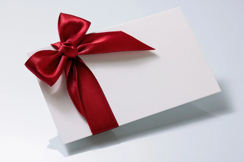 White gift card with red satin ribbon bow on light surface