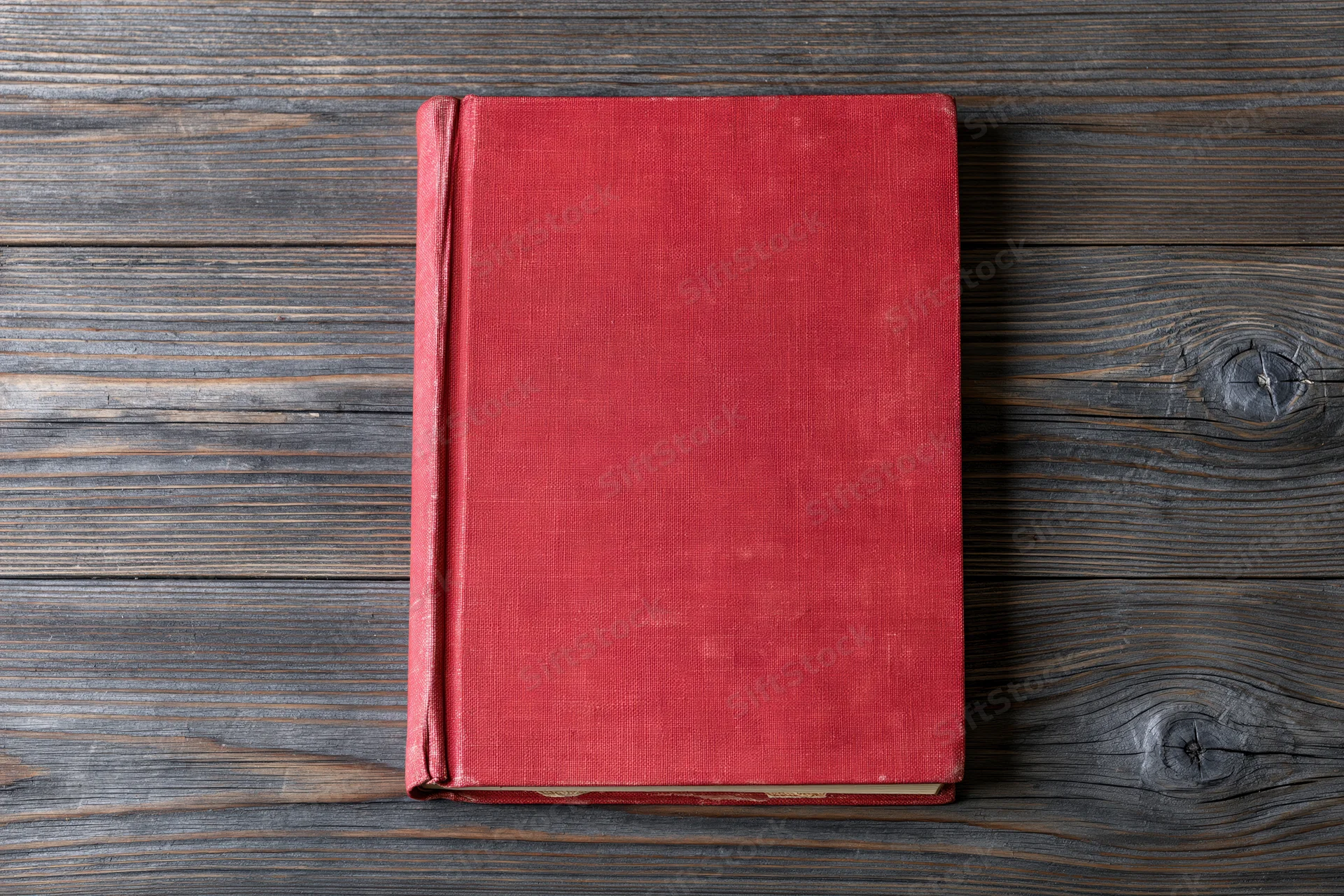 Worn red hardcover book lying flat on rustic wooden surface