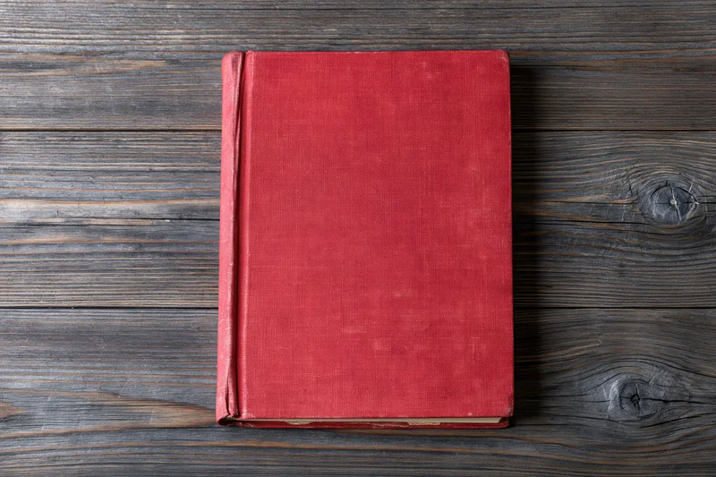 Worn red hardcover book lying flat on rustic wooden surface
