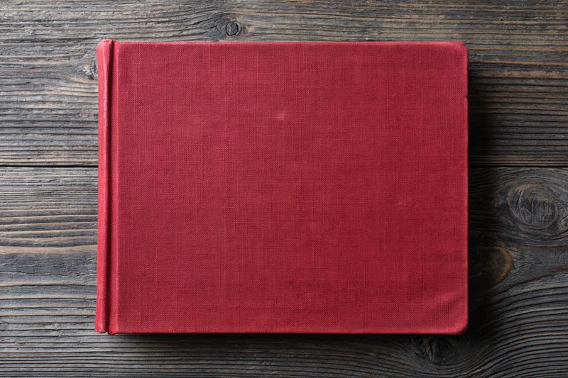 Closed red hardcover book lying flat on rustic wooden surface