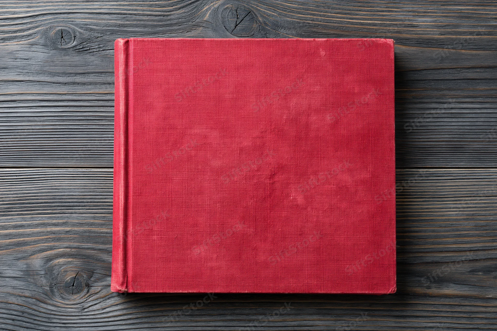 Worn red hardcover book lying flat on rustic wooden surface