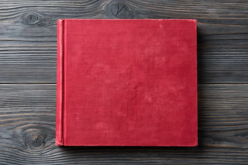 Worn red hardcover book lying flat on rustic wooden surface
