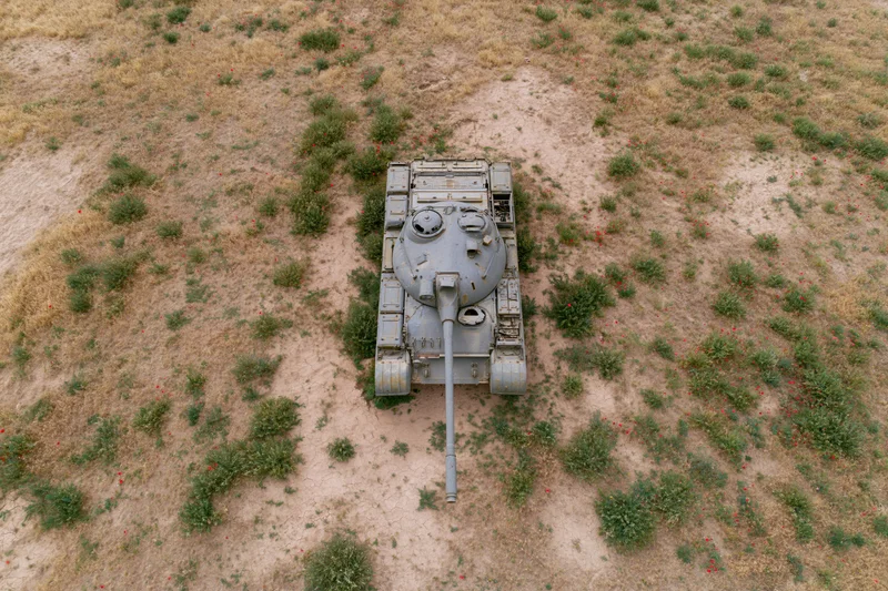 Aerial top-down view of a gray military tank on dry grassy field with scattered red poppies