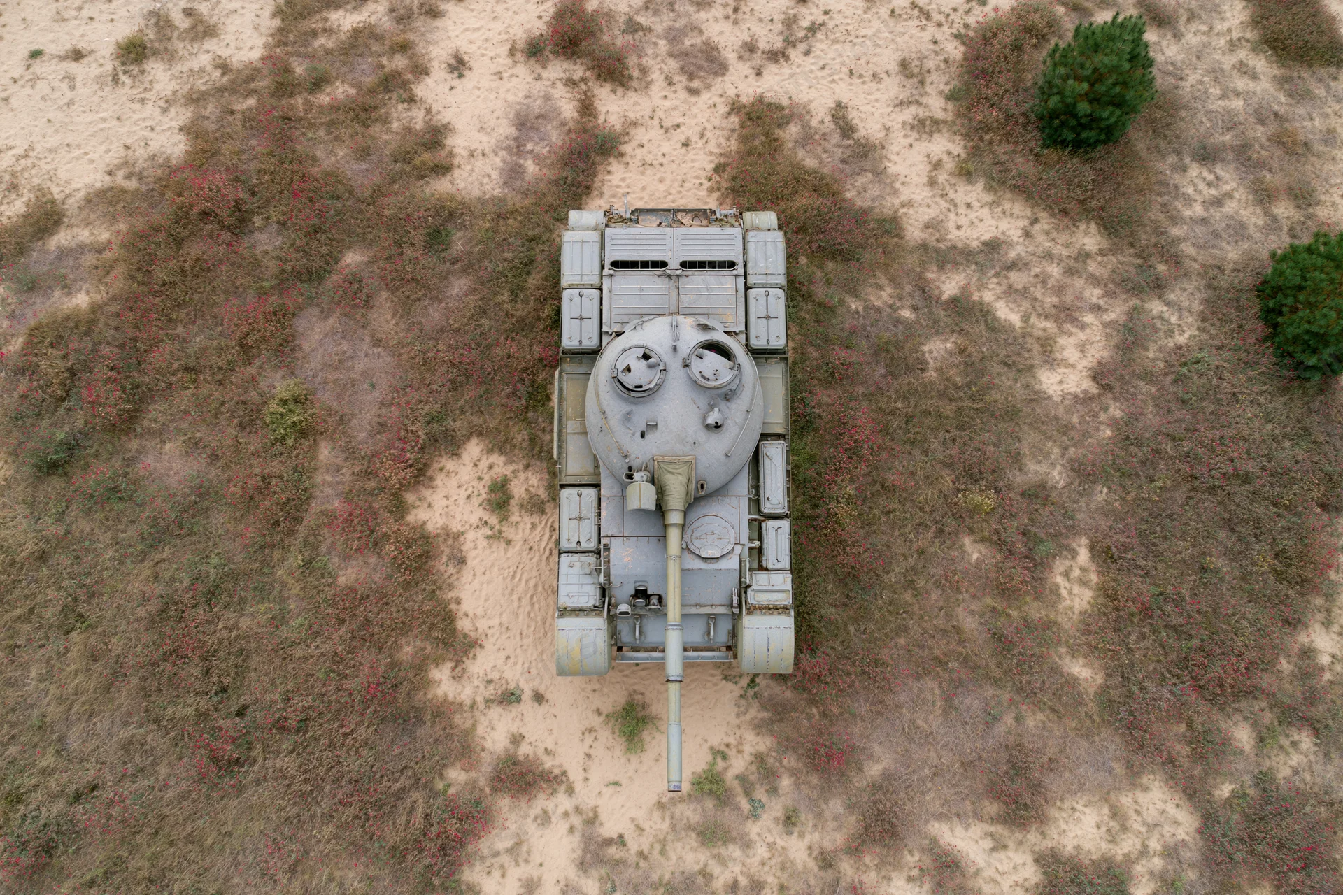 Aerial top-down view of a gray military tank on arid desert terrain with sparse vegetation
