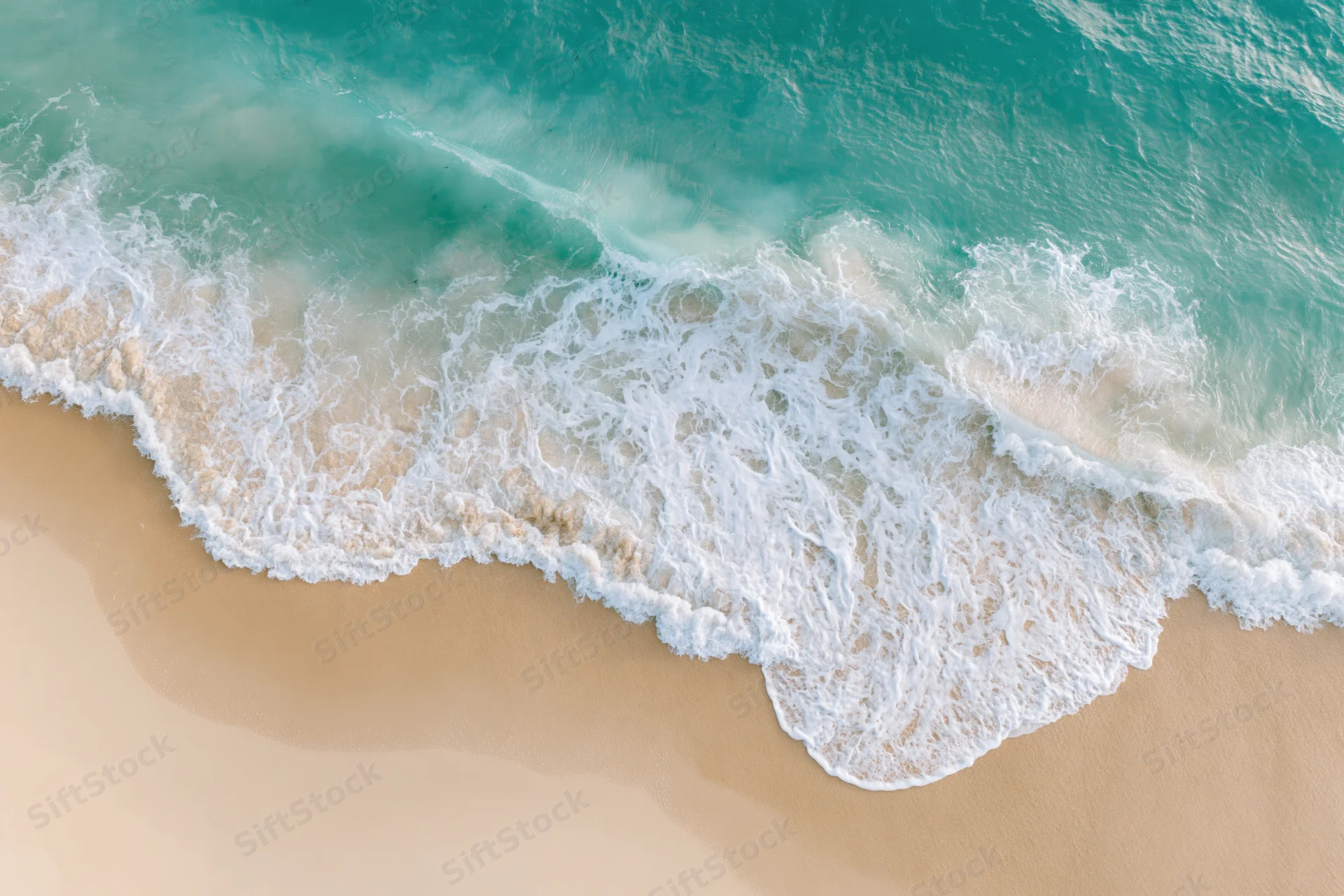 Aerial view of turquoise ocean waves breaking on a sandy beach