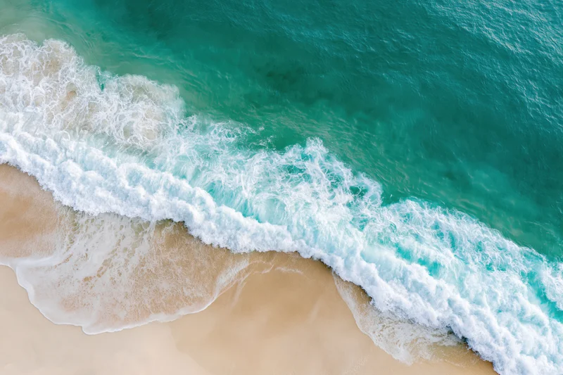Aerial view of turquoise ocean waves breaking on a sandy tropical beach
