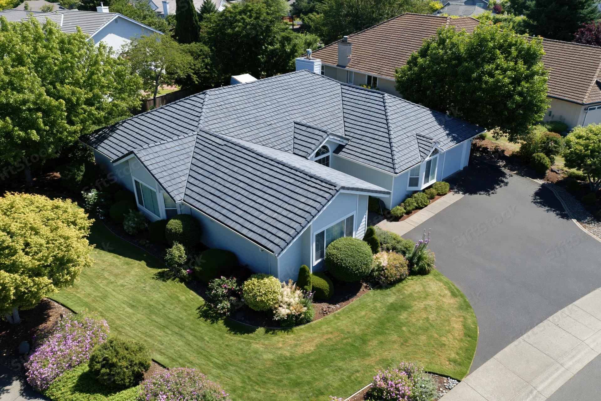 Aerial drone view of a light blue single-story suburban house with shingled roof and landscaped front yard