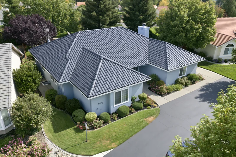 Aerial drone view of a light blue single-story suburban house with tiled roof and landscaped front yard