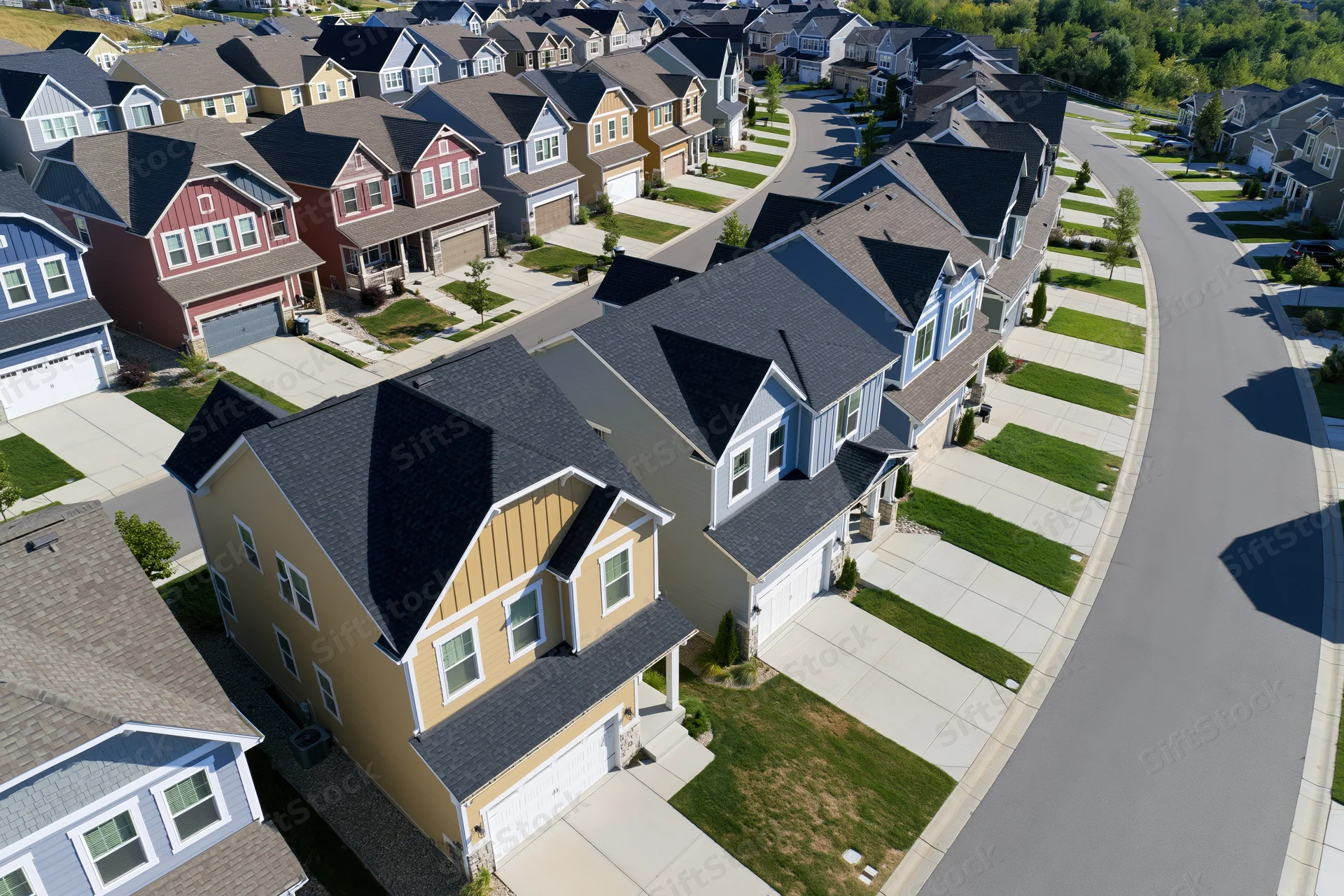 Aerial view of newly built suburban homes arranged along curving streets with front lawns and garages