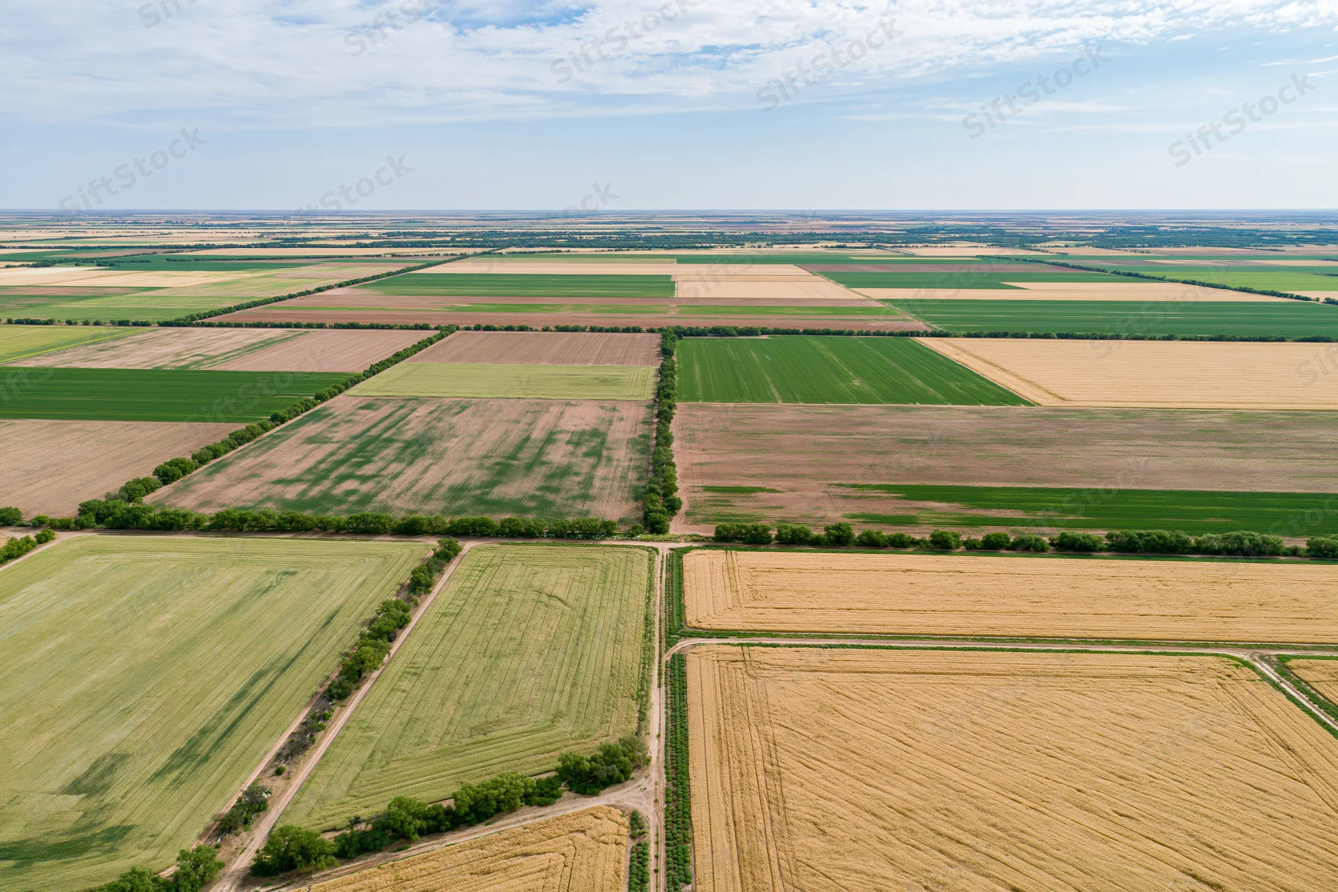Aerial drone view of patchwork farmland with green and golden fields under a partly cloudy sky