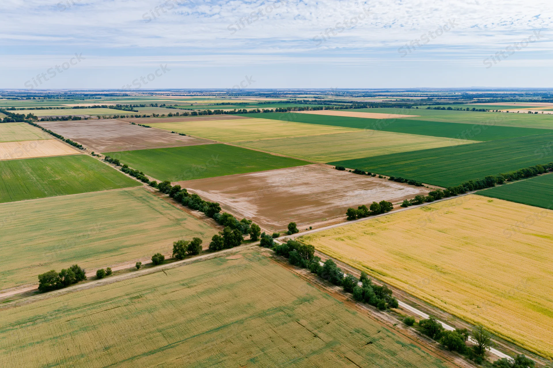Aerial drone view of patchwork farmland with green, yellow and brown fields under a partly cloudy sky