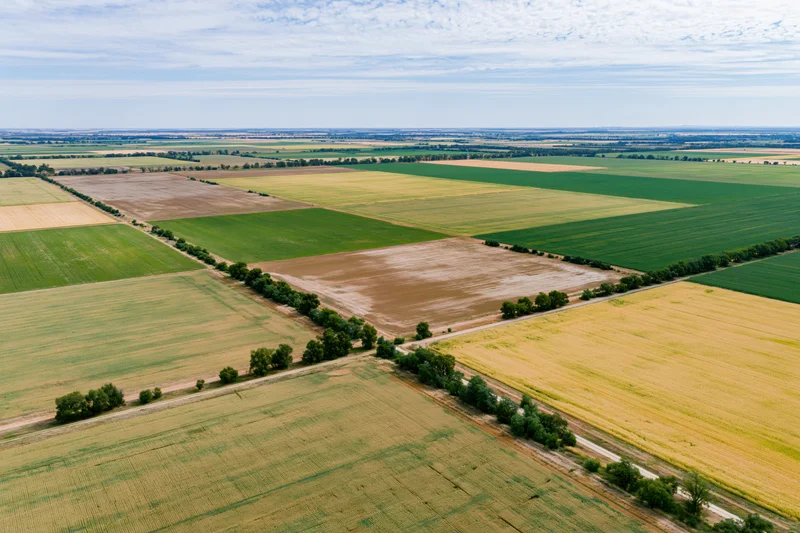 Aerial drone view of patchwork farmland with green, yellow and brown fields under a partly cloudy sky