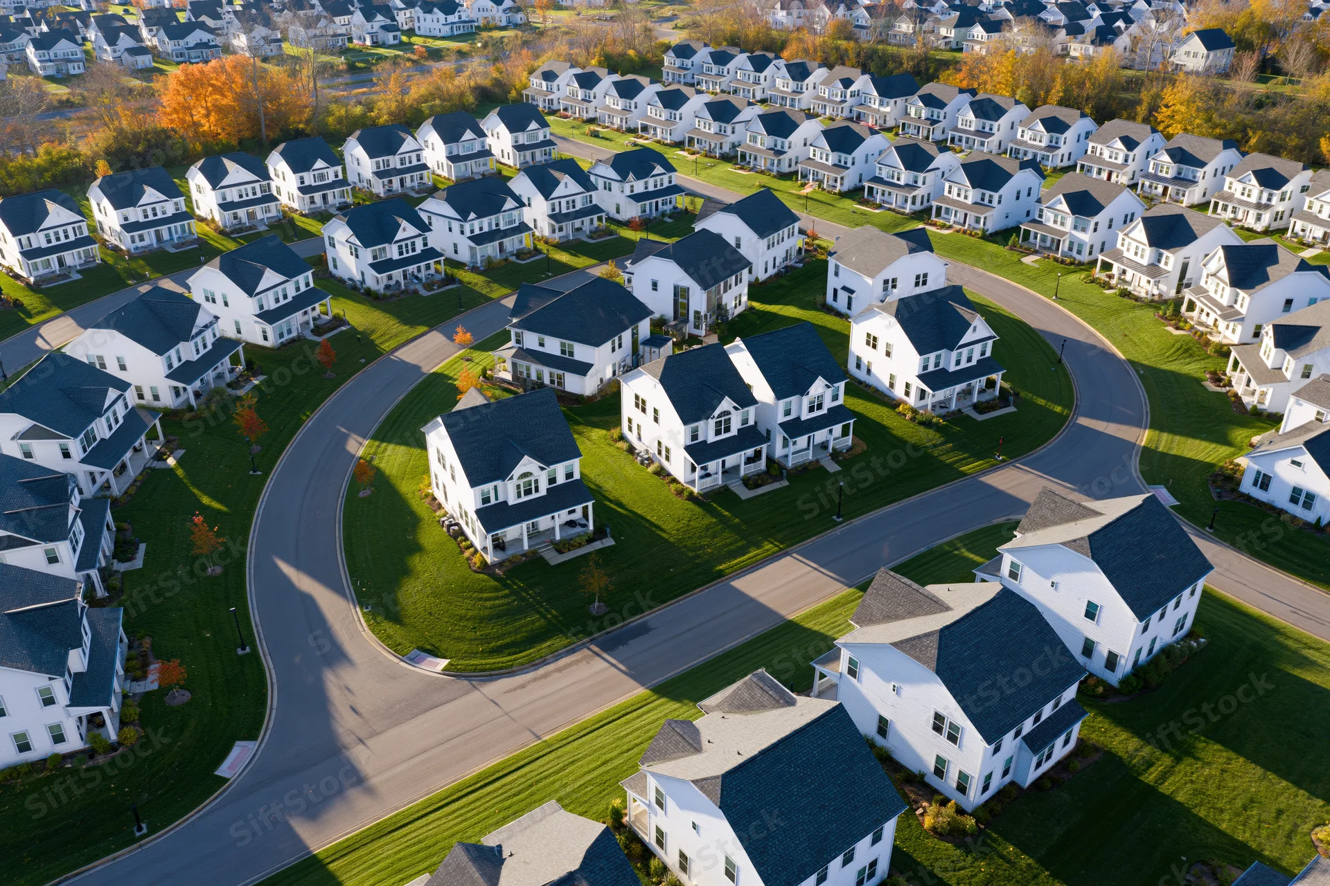 Aerial drone view of a new suburban neighborhood with white houses and curving streets surrounded by autumn trees