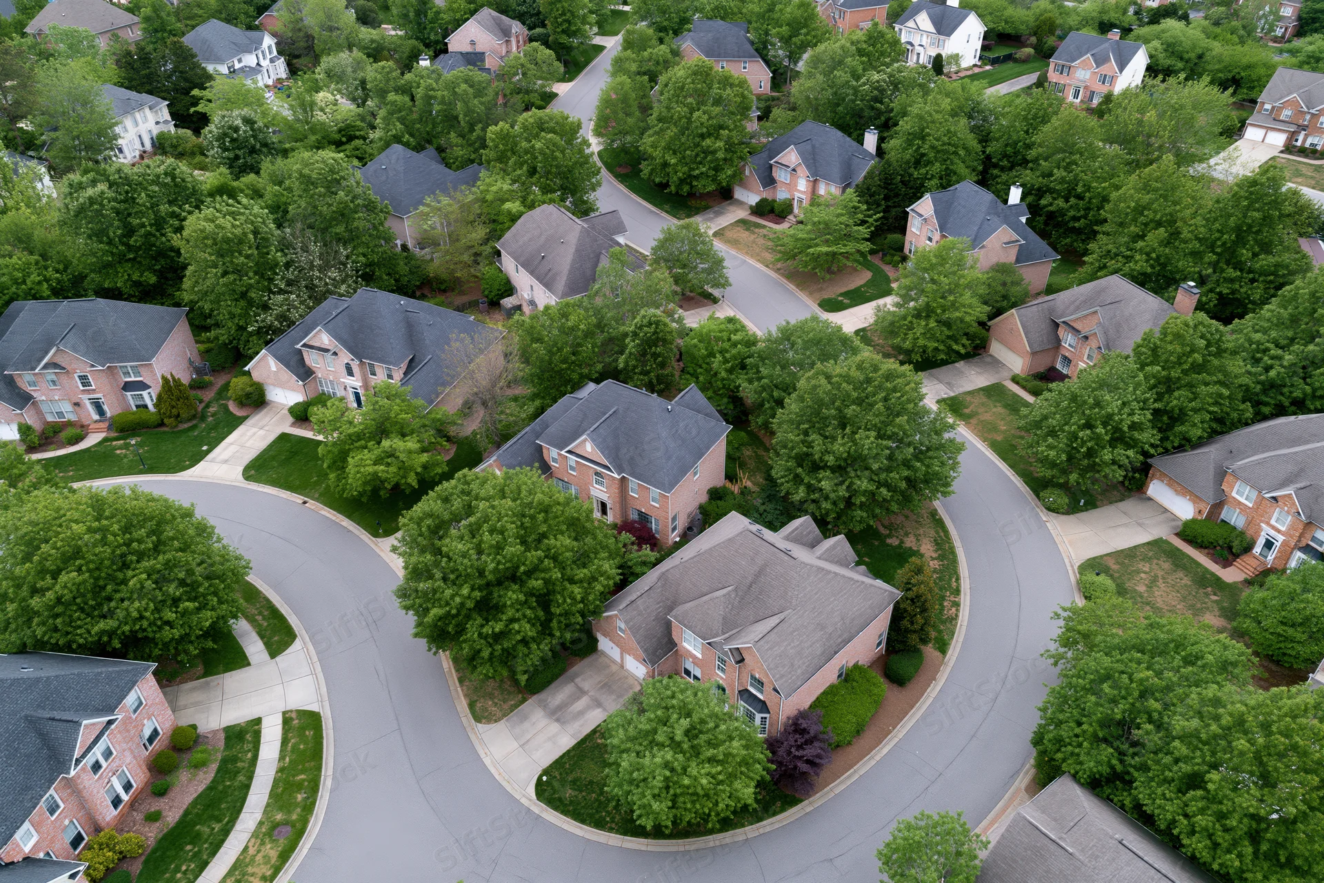 Aerial drone view of suburban neighborhood with brick houses, curving streets, and green lawns