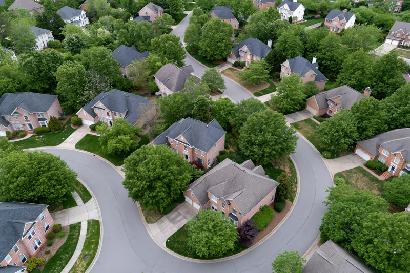 Aerial drone view of suburban neighborhood with brick houses, curving streets, and green lawns