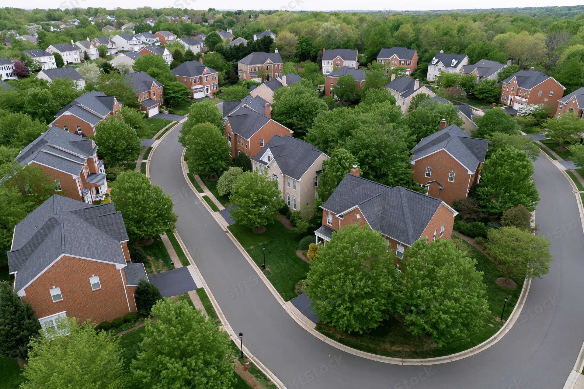 Aerial view of an upscale american suburban neighborhood with curving streets and brick houses surrounded by green trees and lawns