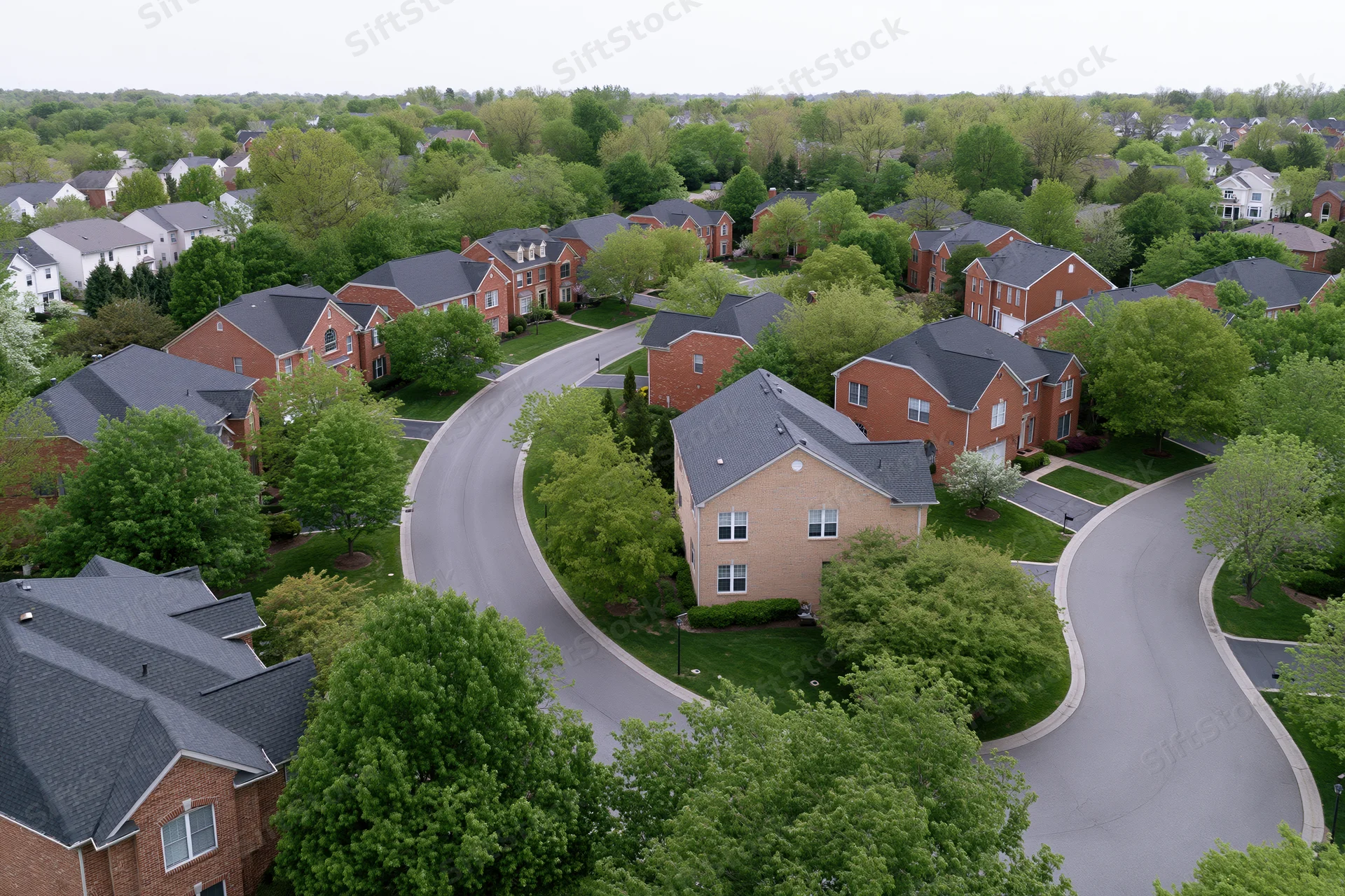 Aerial view of a suburban neighborhood with winding roads and brick houses surrounded by green trees and lawns