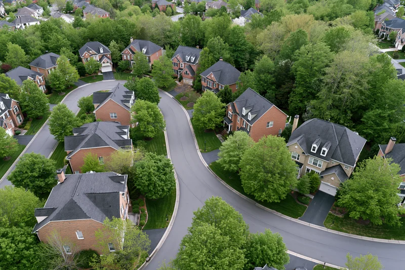 Aerial view of a curving street lined with brick houses and green trees in an upscale suburban neighborhood