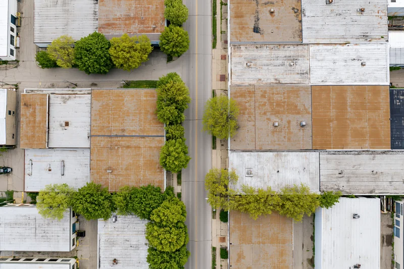 Aerial top-down view of aging industrial buildings and trees lining a street in an urban district