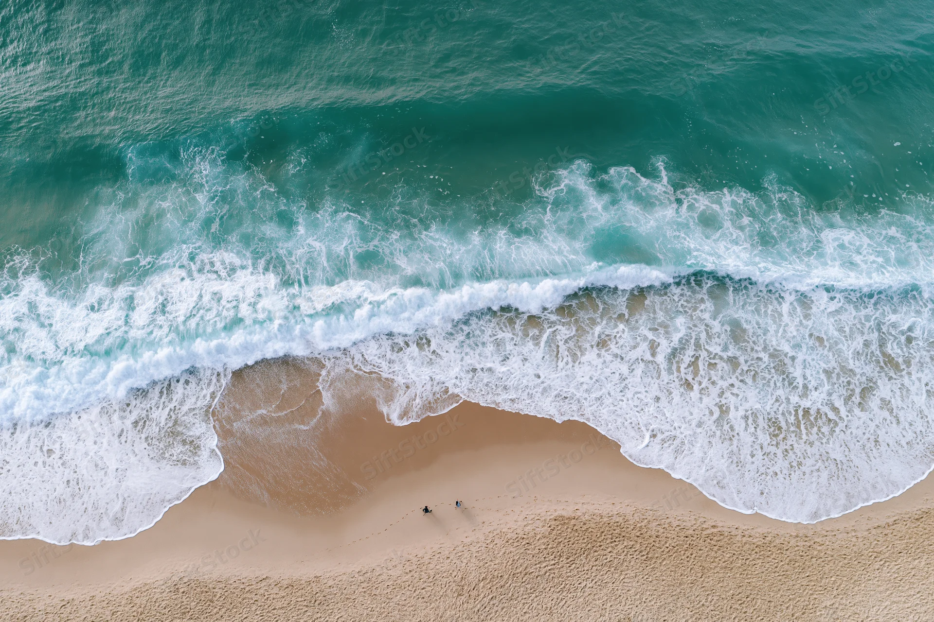 Aerial top-down view of ocean waves breaking on sandy beach with two people walking along shore