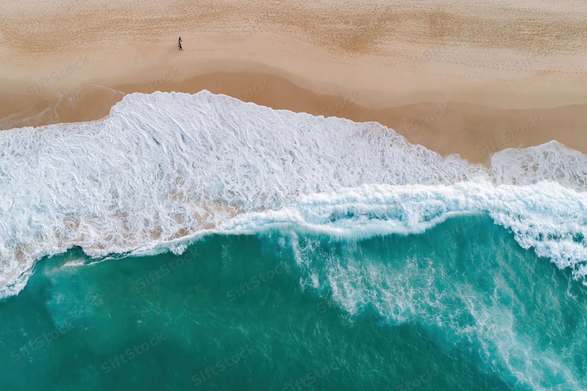 Aerial top-down view of turquoise ocean waves breaking on sandy beach with solitary person walking in distance