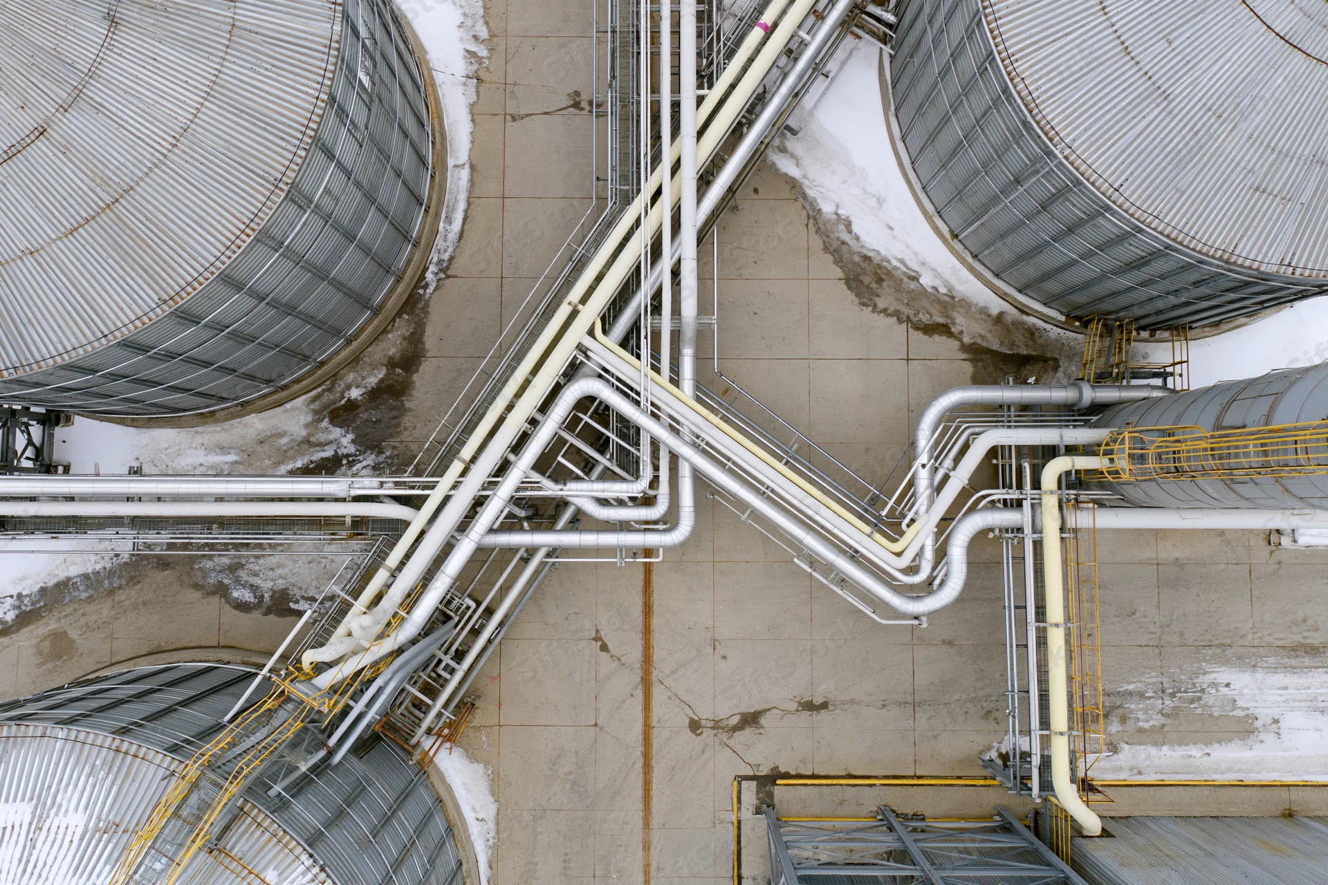 Aerial top-down view of industrial storage tanks and interconnected pipelines on snowy ground