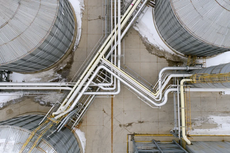 Aerial top-down view of industrial storage tanks and interconnected pipelines on snowy ground