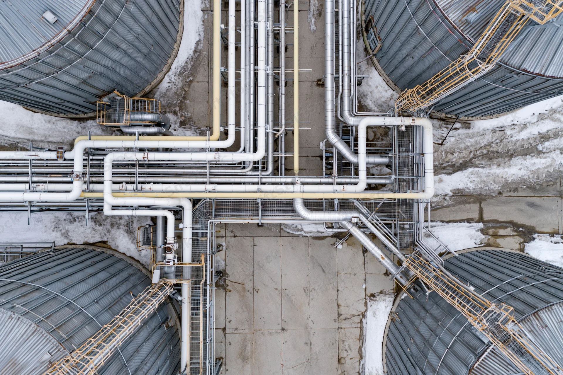 Aerial top-down view of industrial silos and interconnected pipelines in a snowy facility
