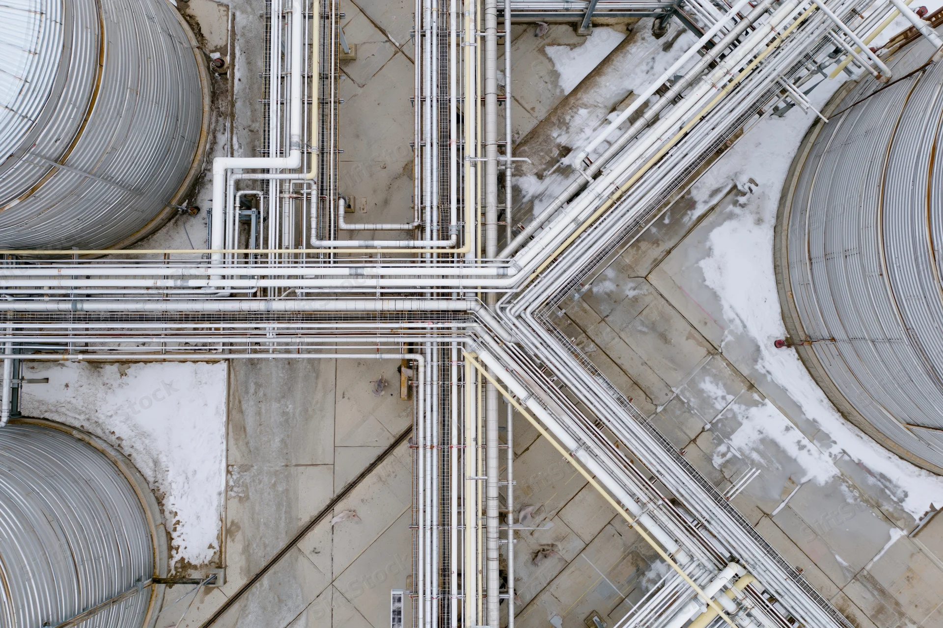 Aerial top-down view of industrial refinery with large storage tanks and intersecting pipelines on snowy ground