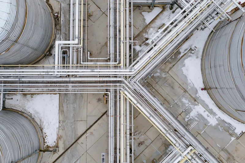 Aerial top-down view of industrial refinery with large storage tanks and intersecting pipelines on snowy ground