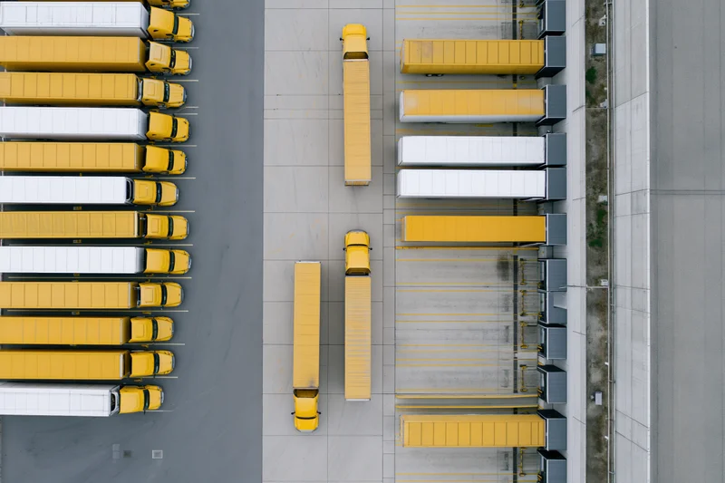 Aerial top-down view of yellow and white trucks parked in rows at a logistics warehouse loading dock