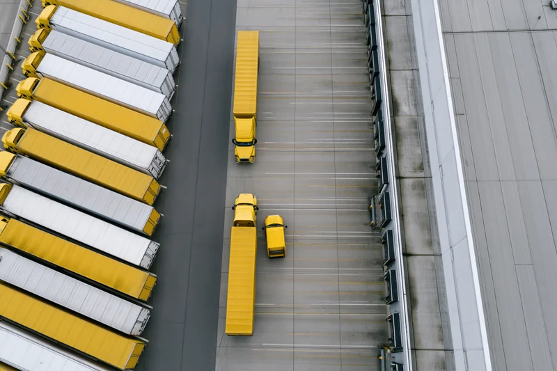 Aerial top-down view of yellow and white trucks parked at loading docks of a large logistics warehouse