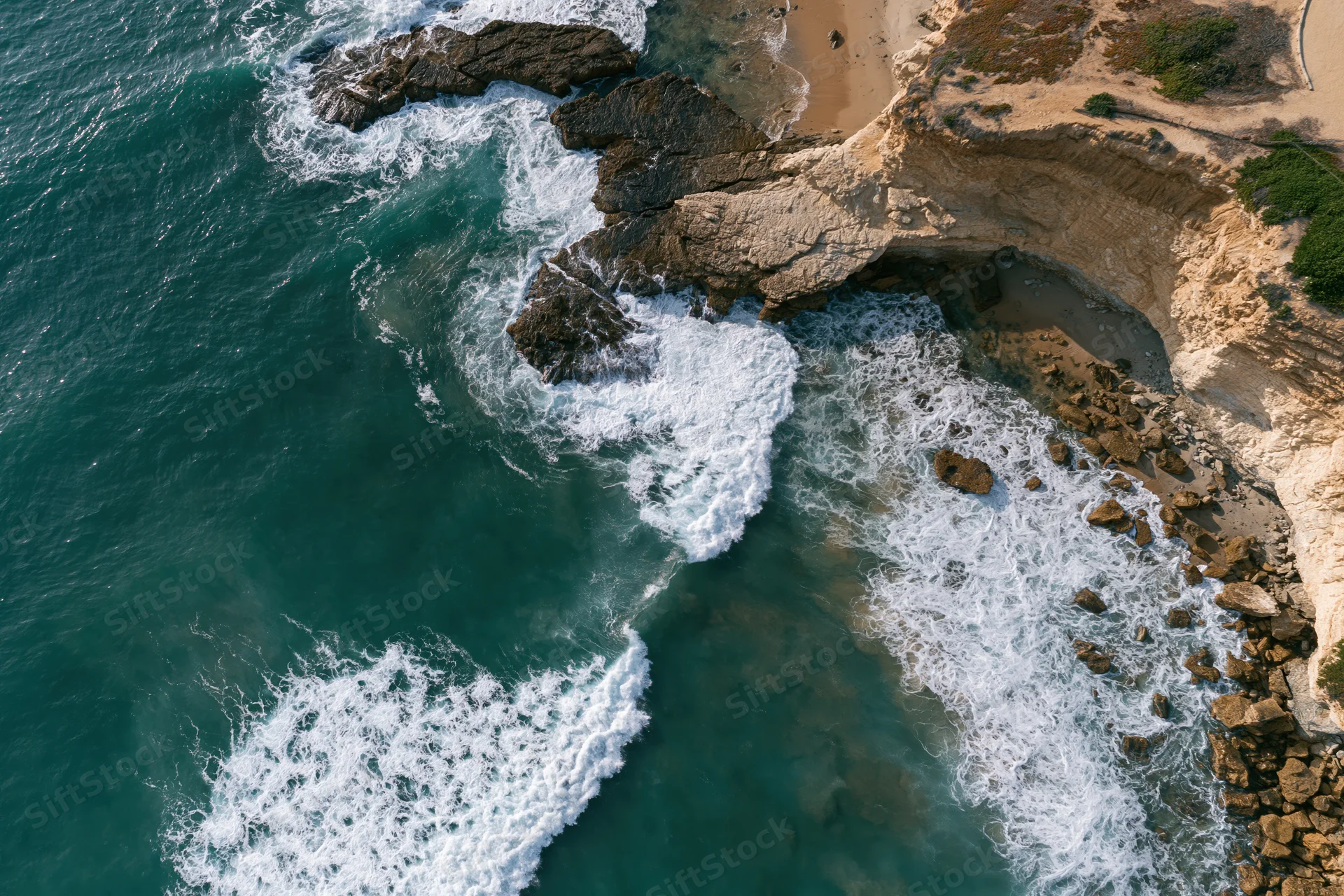 Aerial top-down view of waves crashing against rocky coastal cliff edge