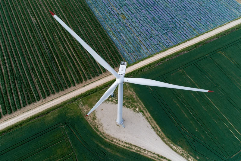 Aerial top-down view of a wind turbine surrounded by agricultural fields and solar panels