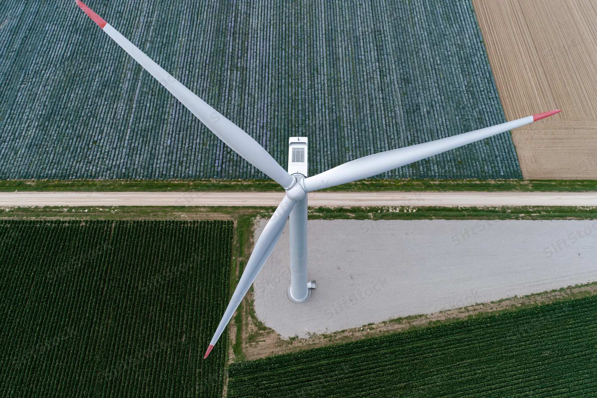 Aerial top-down view of a single wind turbine in a cultivated agricultural field
