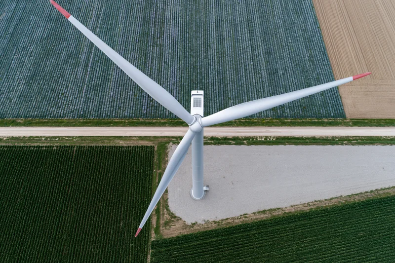 Aerial top-down view of a single wind turbine in a cultivated agricultural field