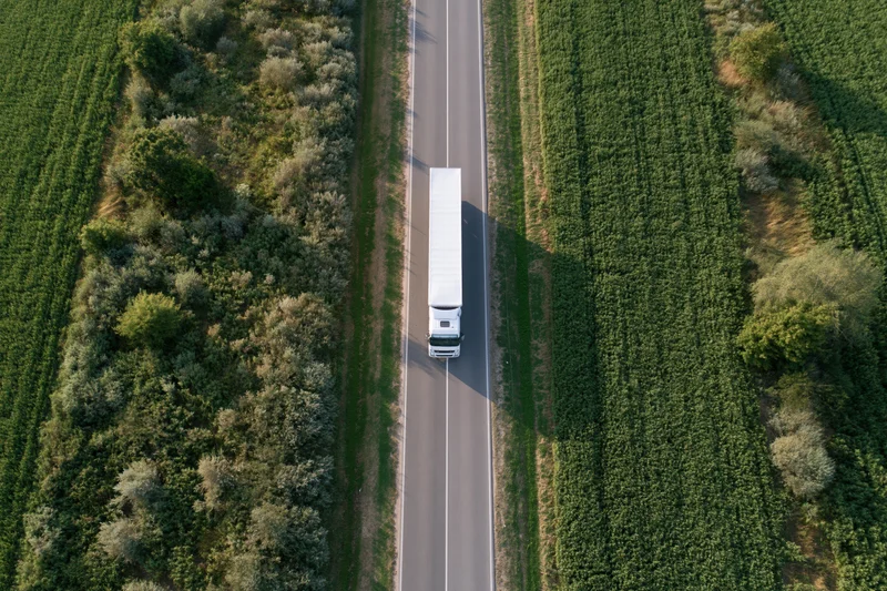 White semi truck driving on a straight highway through green farmland fields