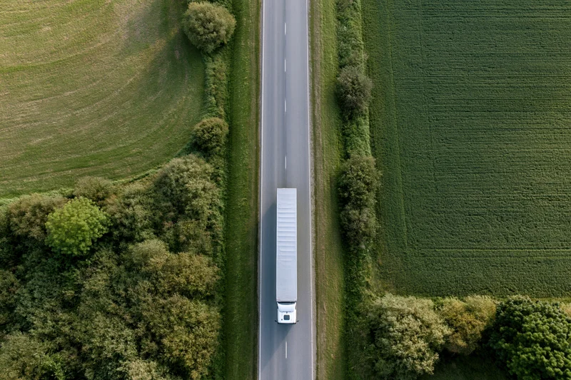 White semi truck driving on a straight highway through rural farmland fields