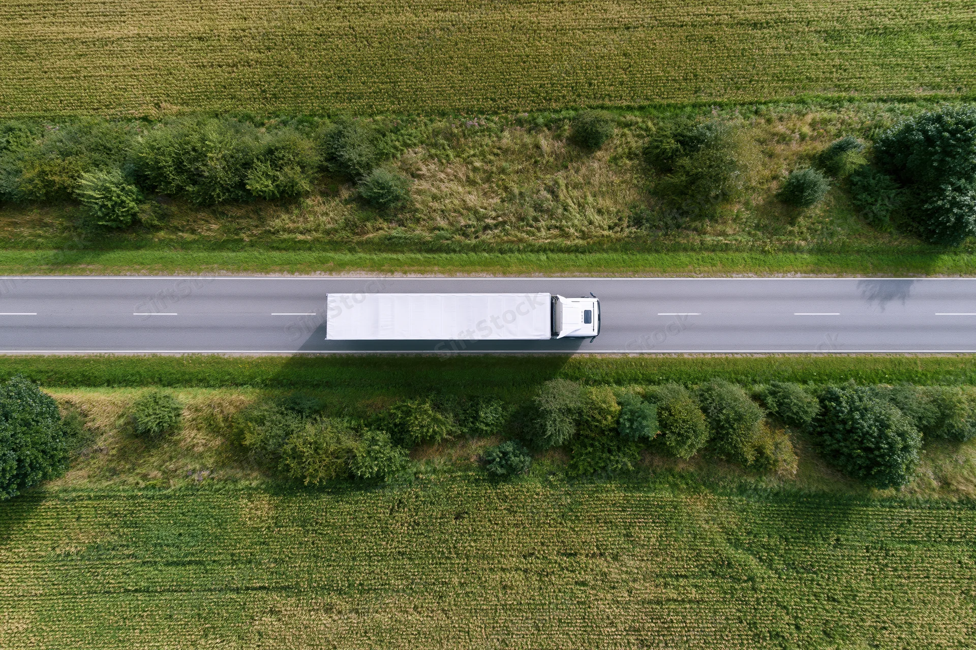 White semi truck driving on highway through rural farmland from aerial top-down view