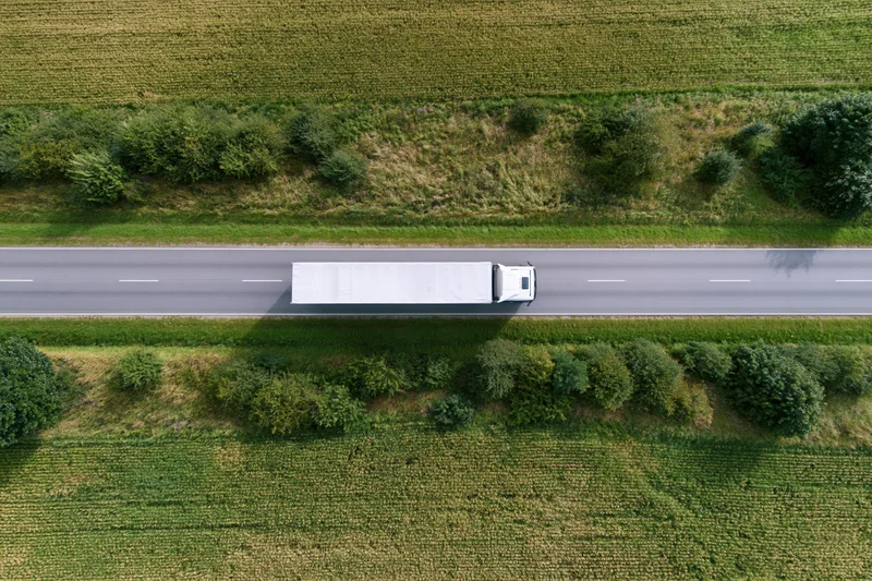 White semi truck driving on highway through rural farmland from aerial top-down view
