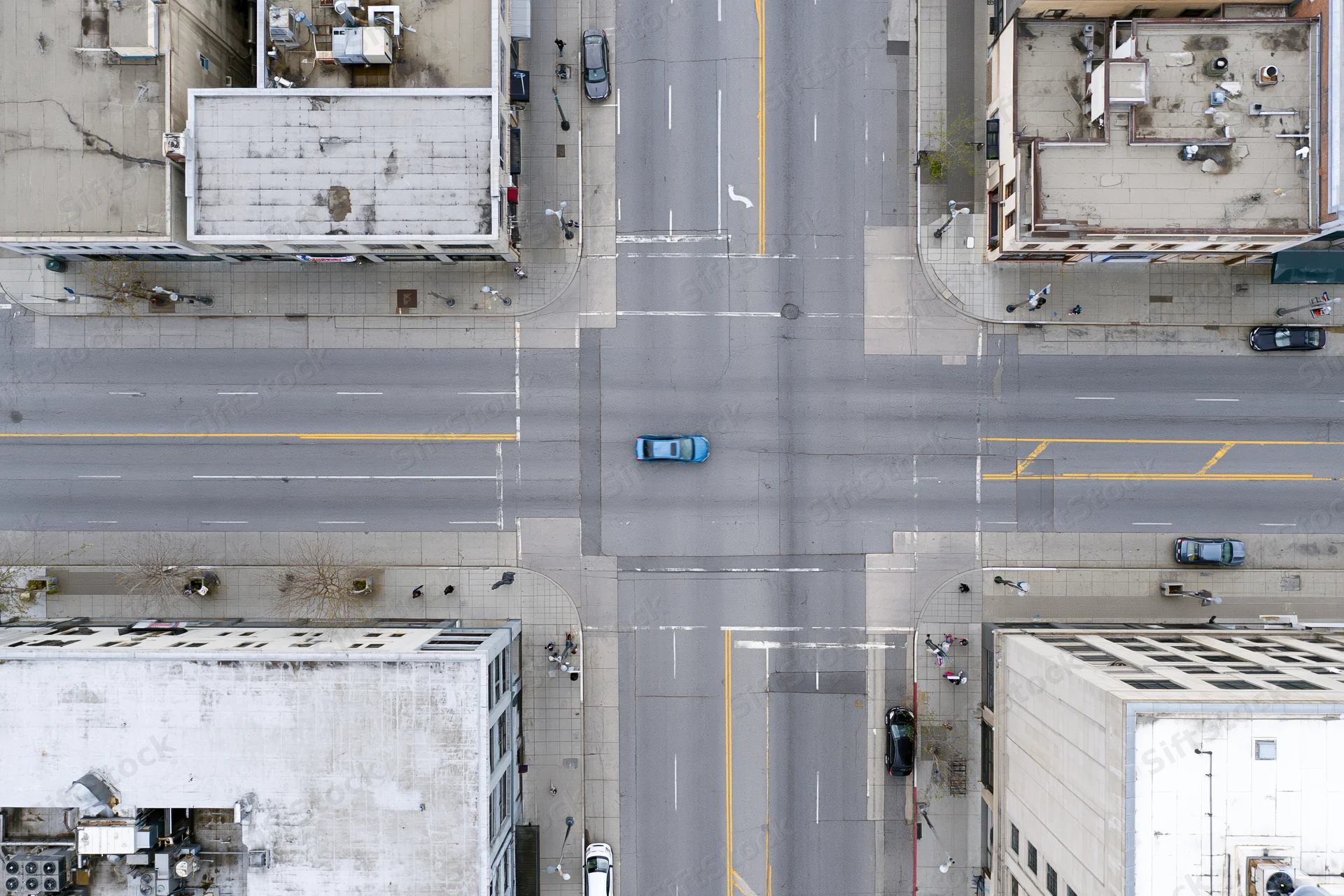 Aerial top-down view of an urban four-way street intersection with vehicles and surrounding buildings