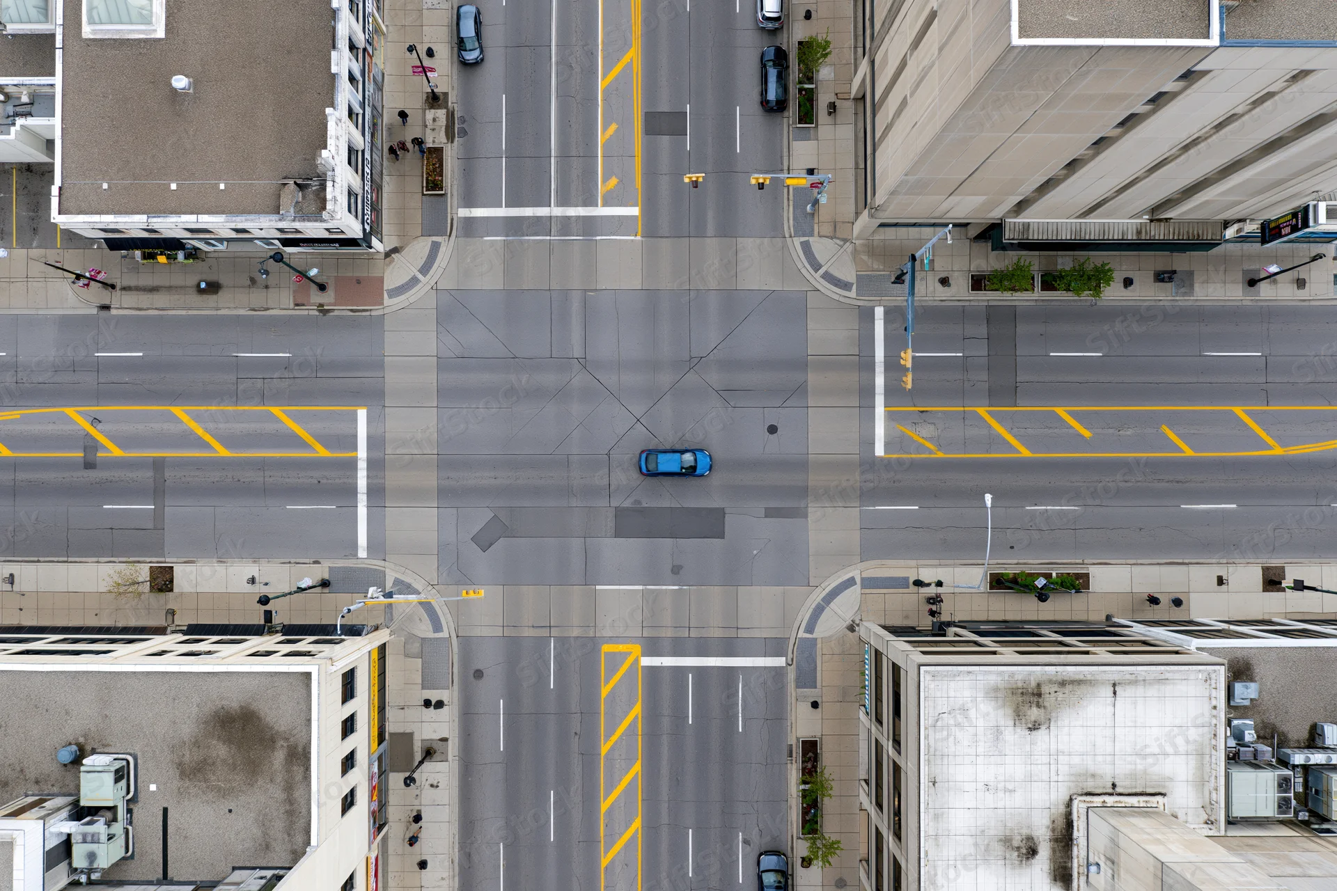 Aerial top-down view of an urban four-way street intersection with vehicles and surrounding buildings