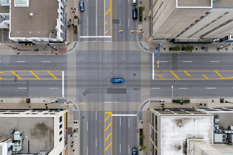 Aerial top-down view of an urban four-way street intersection with vehicles and surrounding buildings