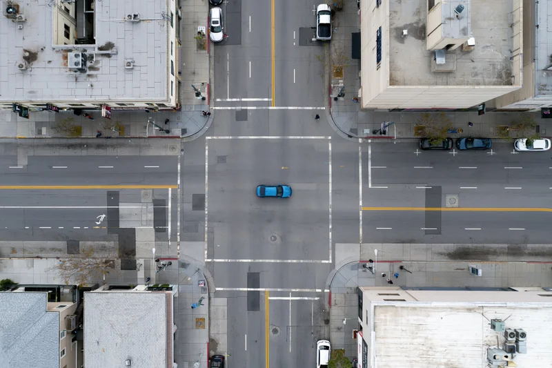 Aerial top-down view of an urban four-way street intersection with vehicles and surrounding buildings