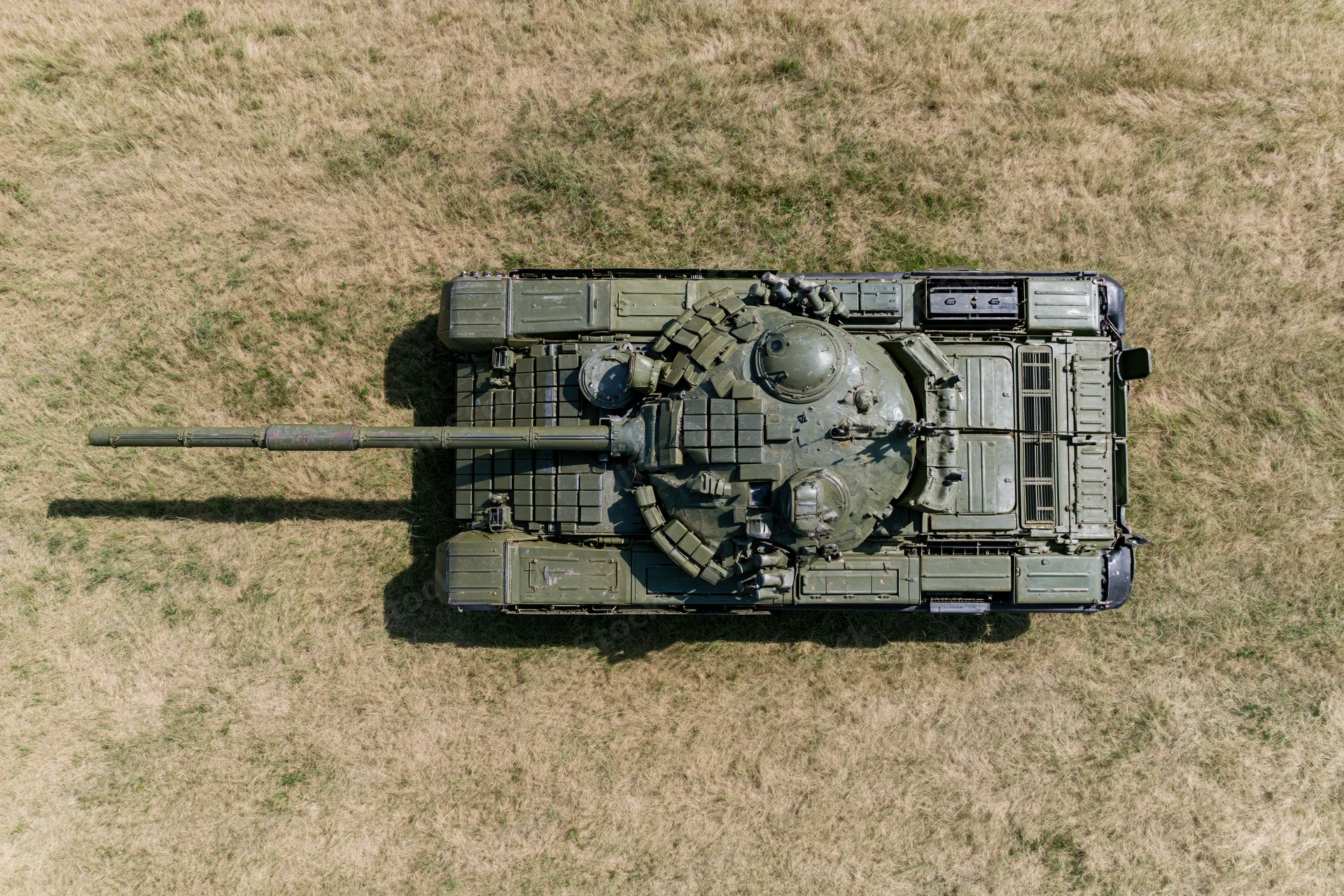 Aerial top-down view of a soviet-era main battle tank parked on dry grass field
