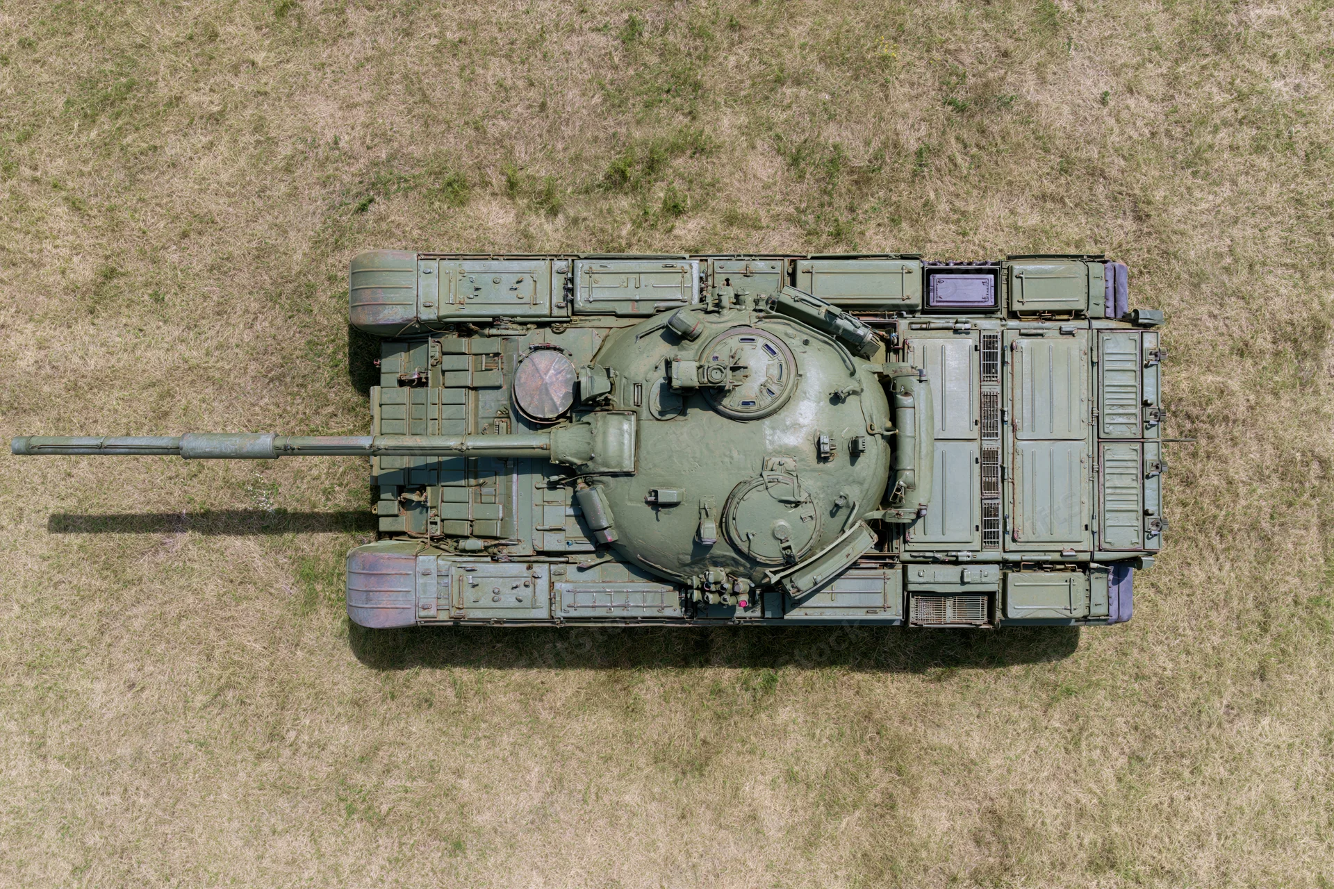 Aerial top-down view of a soviet-era main battle tank parked on dry grass field