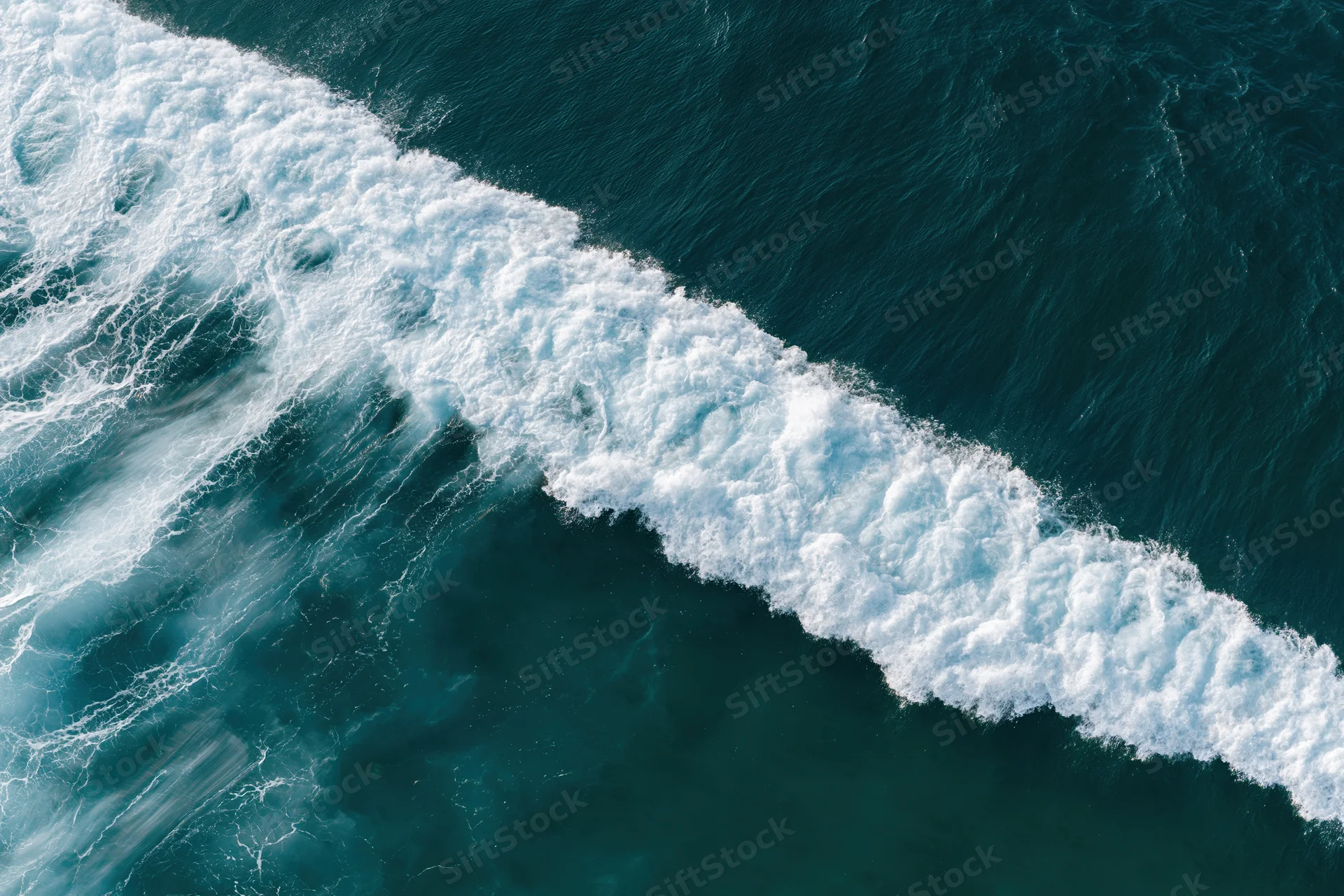 Aerial top-down view of a breaking ocean wave with white foam and swirling water